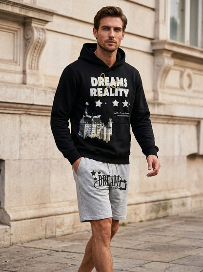 Man wearing a black hoodie with 'Dreams Create Reality' text and gray shorts, standing in front of a stone building.